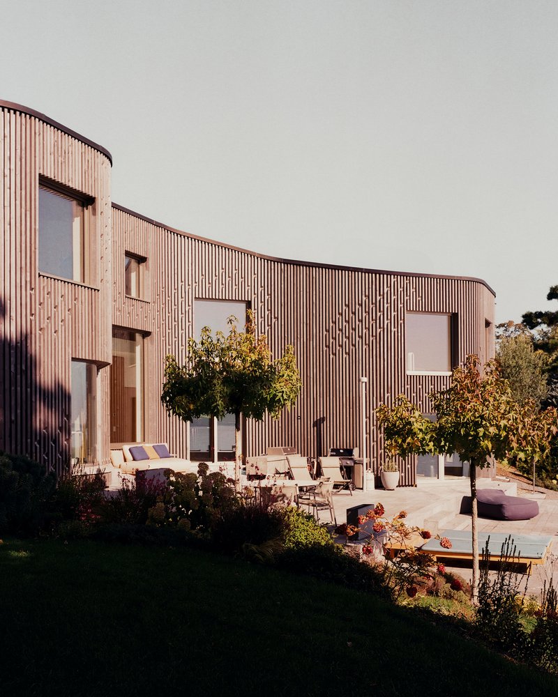 Courtyard terrace with outdoor furniture and planted beds against the curved timber facade