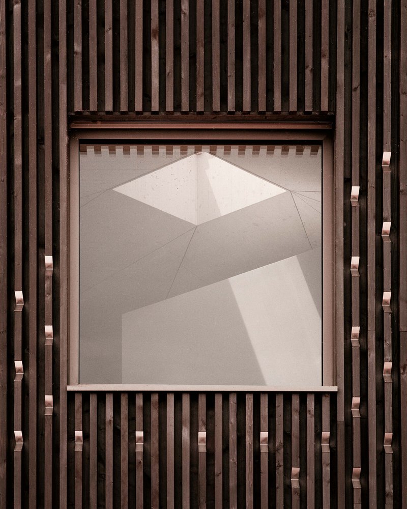 Recessed window framed by vertical timber slats with angular shadow patterns on the ceiling