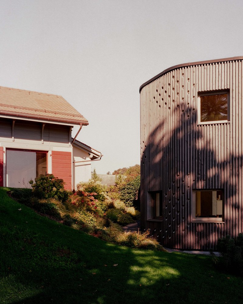 Curved timber-clad addition adjacent to the original gabled structure on a sloping lawn at sunset