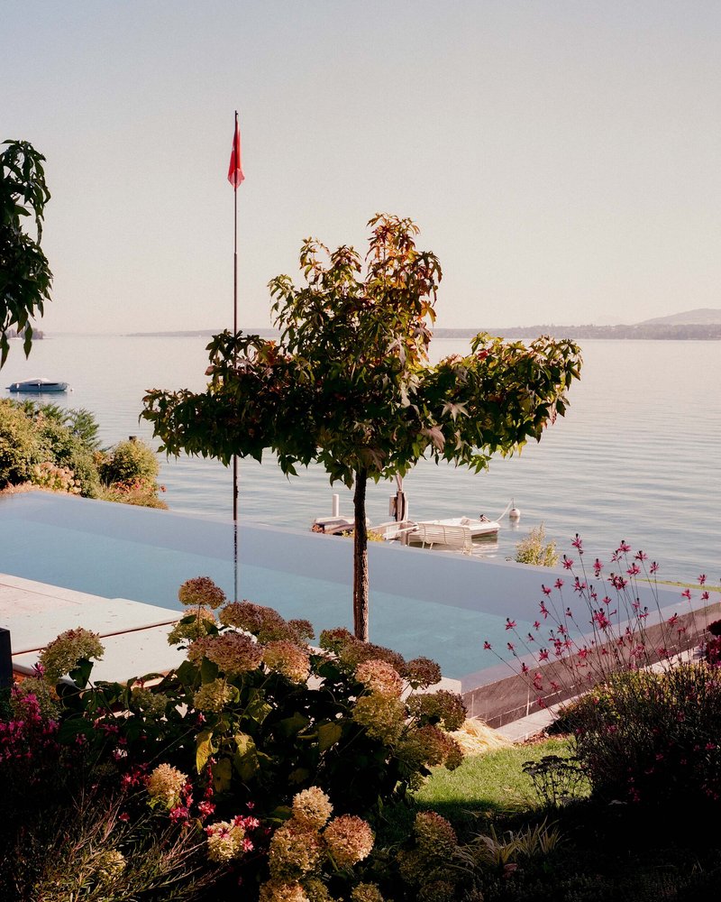 Infinity pool edge with flowering shrubs and ornamental trees overlooking a calm lake at dusk