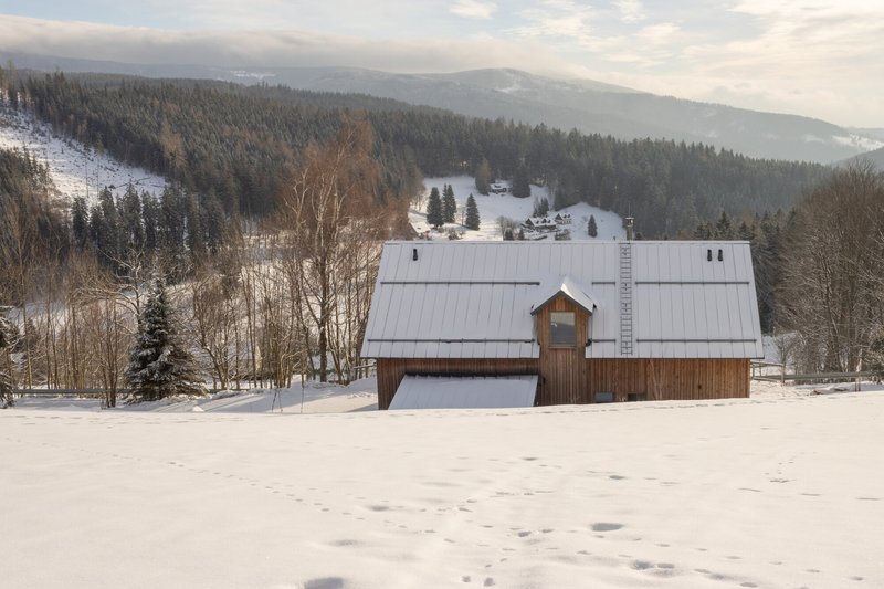 Gable end with standing seam metal roof and timber cladding set in a snow-covered meadow