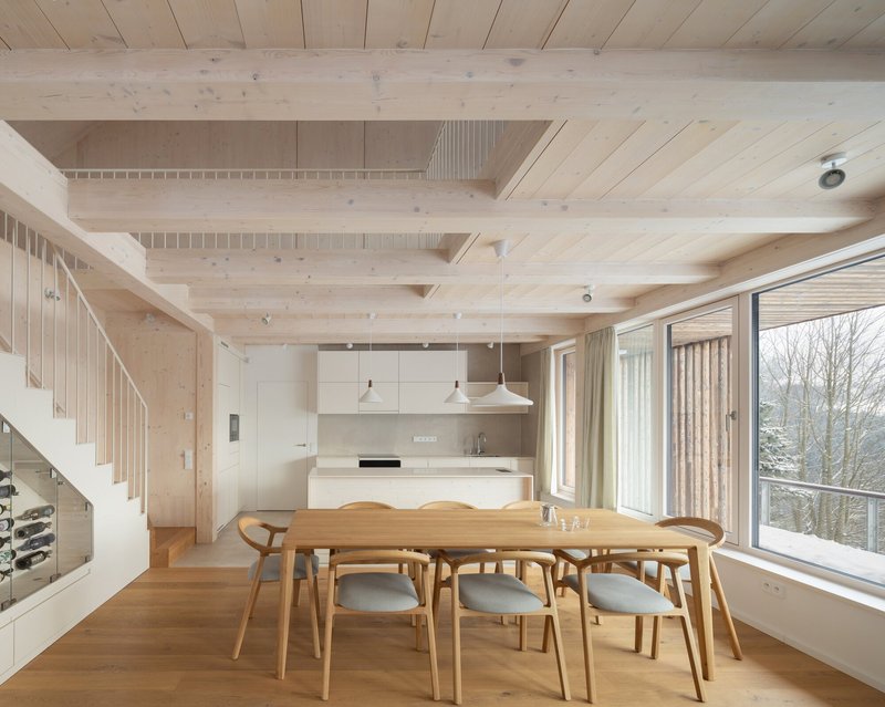 Dining area with timber table under exposed beam ceiling and full-height windows overlooking bare winter trees
