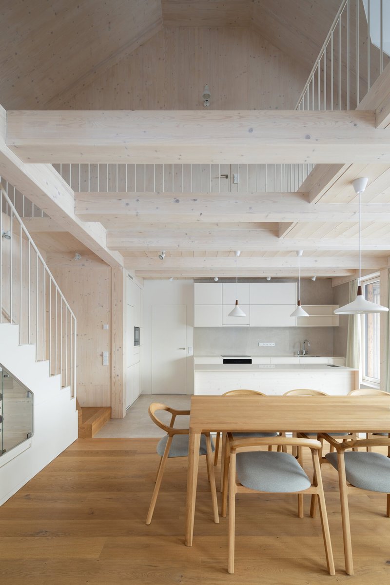 Open dining and kitchen space with timber staircase, exposed ceiling beams, and mezzanine gallery with vertical railings