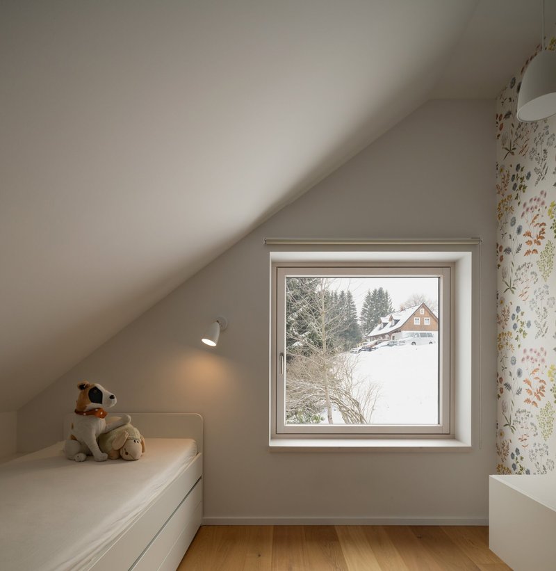 Bedroom window framing a snow-covered landscape with a neighboring timber house visible through the trees