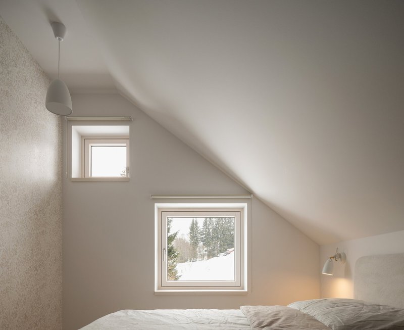 Bedroom with two staggered windows under a sloped ceiling revealing snowy forest views outside