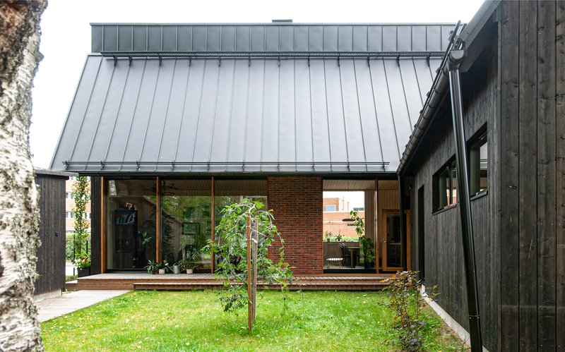 Courtyard view showing charred timber cladding, standing seam metal roof, and young tree in lawn