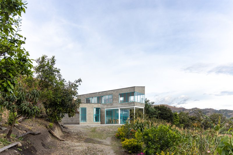 Two-story residence with concrete walls and glass facades on a hillside amid scattered vegetation