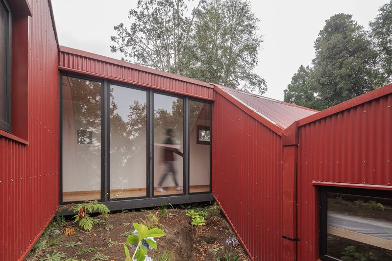 Glazed corner opening in corrugated metal cladding with a figure visible inside and plantings below