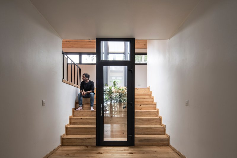 Timber staircase with a person seated midway and glazed door opening to planted courtyard beyond