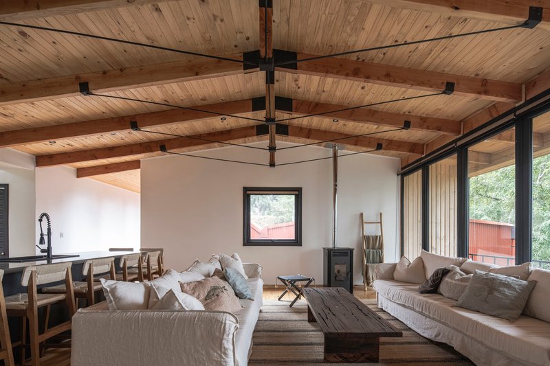 Open living space with exposed timber beams and planked ceiling above white walls and corner glazing