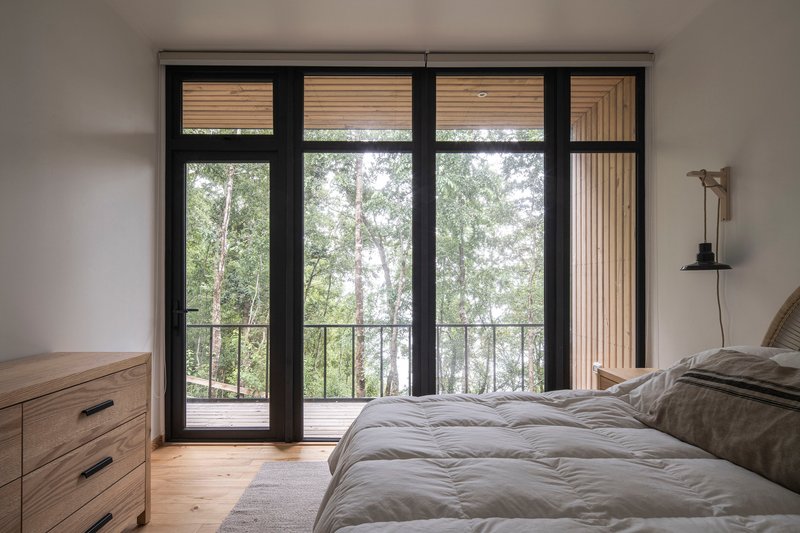 Bedroom with black-framed glass doors opening to a railed balcony in diffused daylight