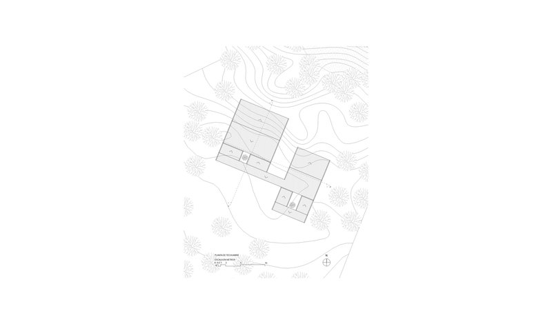Roof plan drawing showing a linear building with angular roof forms nestled among contour lines and trees