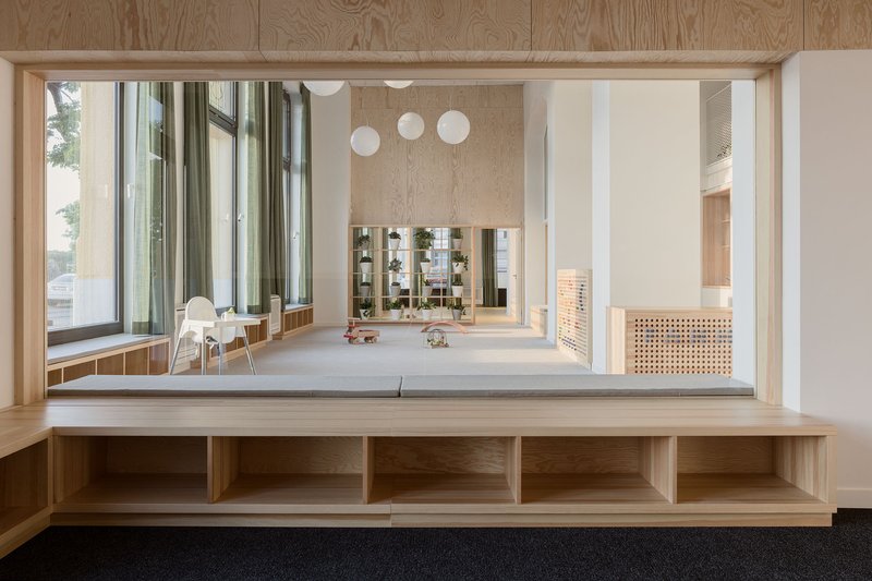 Oak framed window opening from upper level overlooking a double-height playroom with pendant lights and floor-to-ceiling windows