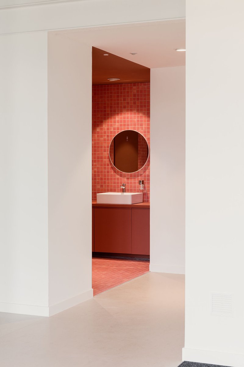 Doorway framing a terracotta-tiled bathroom alcove with circular mirror and white vessel sink