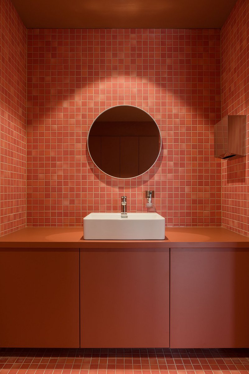 Terracotta tile vanity wall with backlit circular mirror above white vessel sink on orange countertop