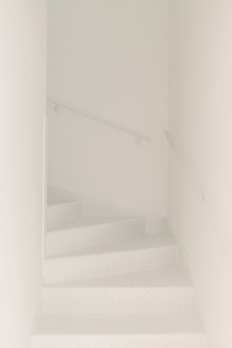 White plastered staircase with thin metal handrail ascending through a narrow enclosed stairwell