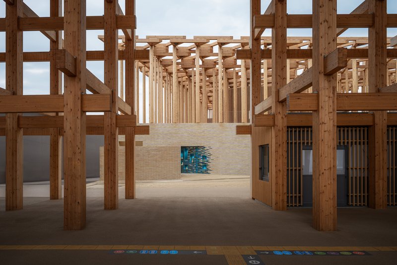 Interior view through timber post-and-beam structure with a blue glazed tile installation in the beige brick wall