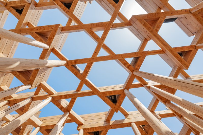 Upward view through a hexagonal timber lattice roof structure against clear sky