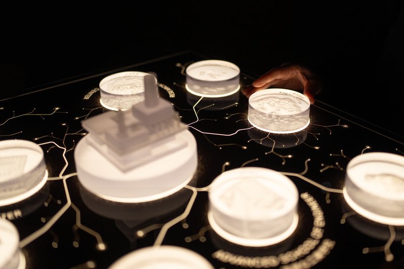 White architectural models displayed on a black contoured base with hand interaction