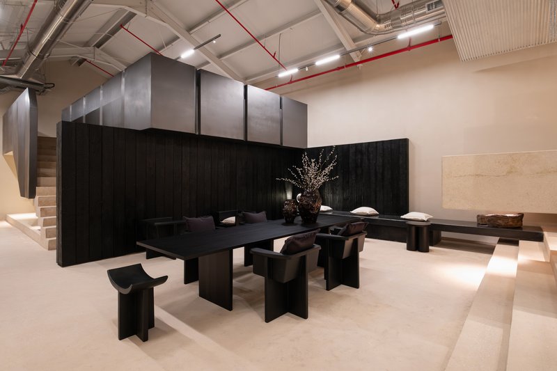 Black timber table and benches against charred wall with branch arrangement under suspended metal panels and ductwork