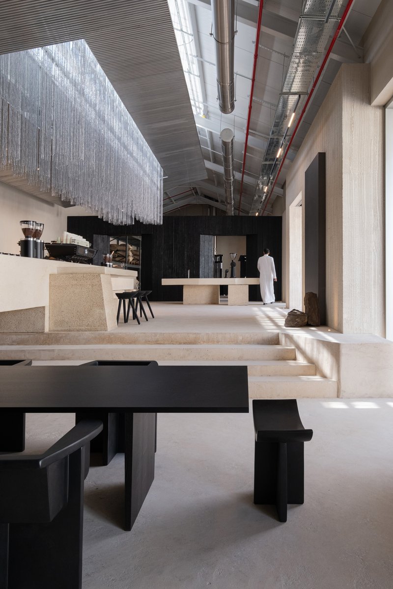 Interior view of tiered terrazzo seating with black tables beneath exposed ductwork and a translucent beaded curtain installation