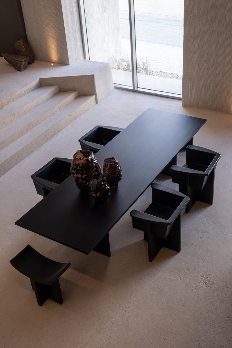Black geometric dining table with integrated bench seating on polished concrete floor beside a glazed opening to the outdoors