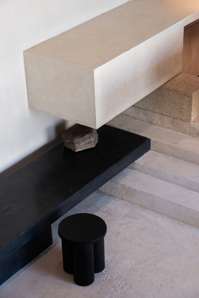 Detail of cantilevered terrazzo bench supported by timber block resting on black steel ledge with polished concrete flooring below