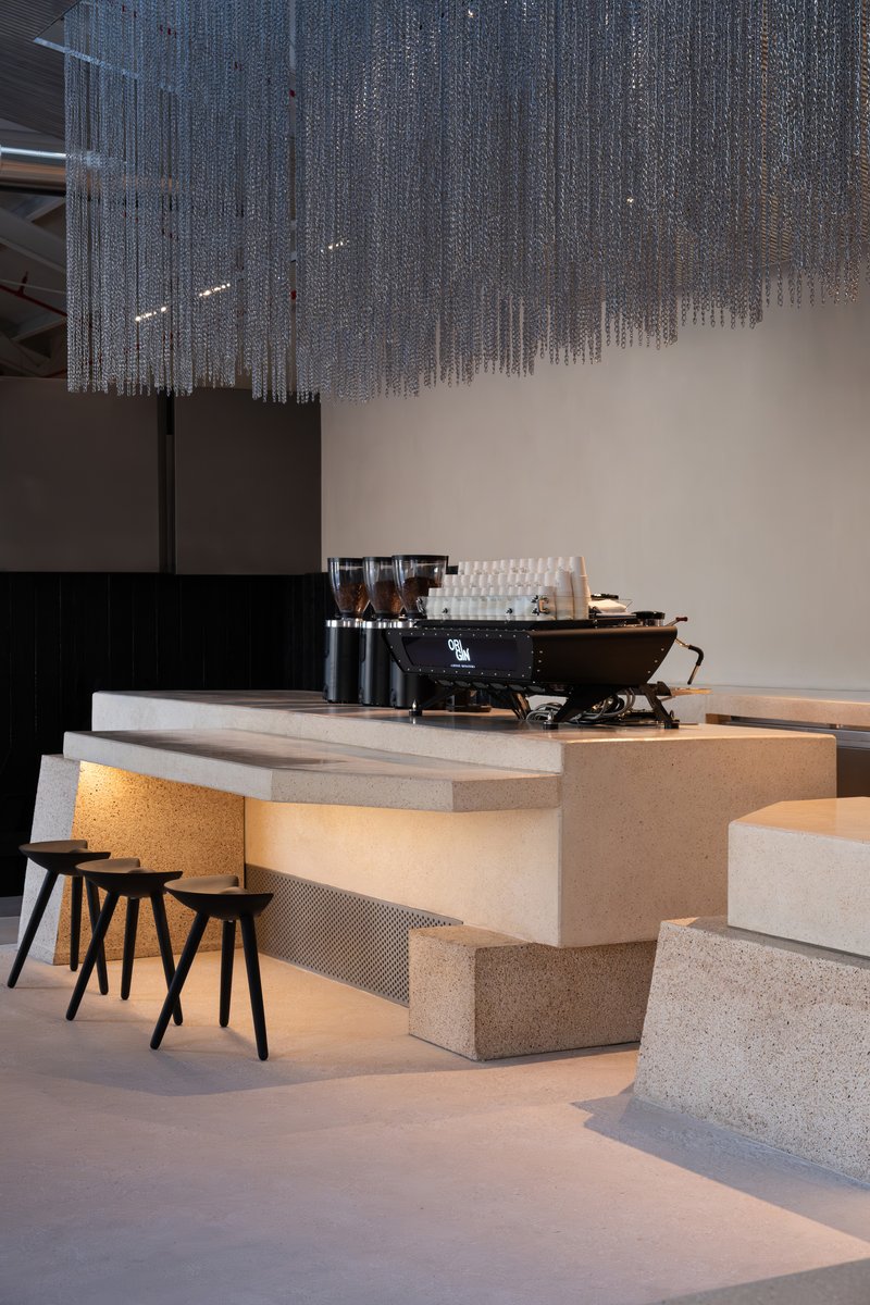 Terrazzo coffee bar counter with integrated warm lighting beneath cascading beaded curtain and espresso machine on top
