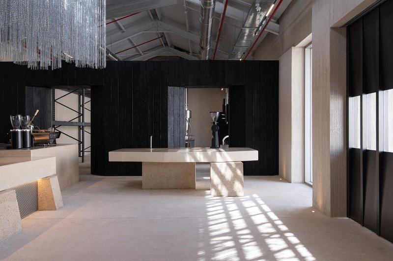 Geometric terrazzo table framed by charred timber walls with sunlight striping the polished concrete floor