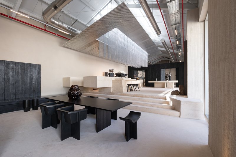 Black timber seating group beside terrazzo steps leading to raised counter area under vaulted industrial ceiling