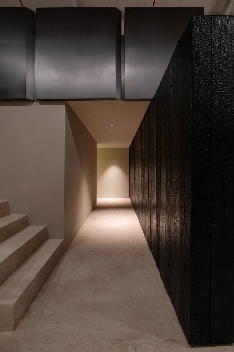 Corridor with charred timber wall panels and recessed ceiling lighting along a polished concrete floor