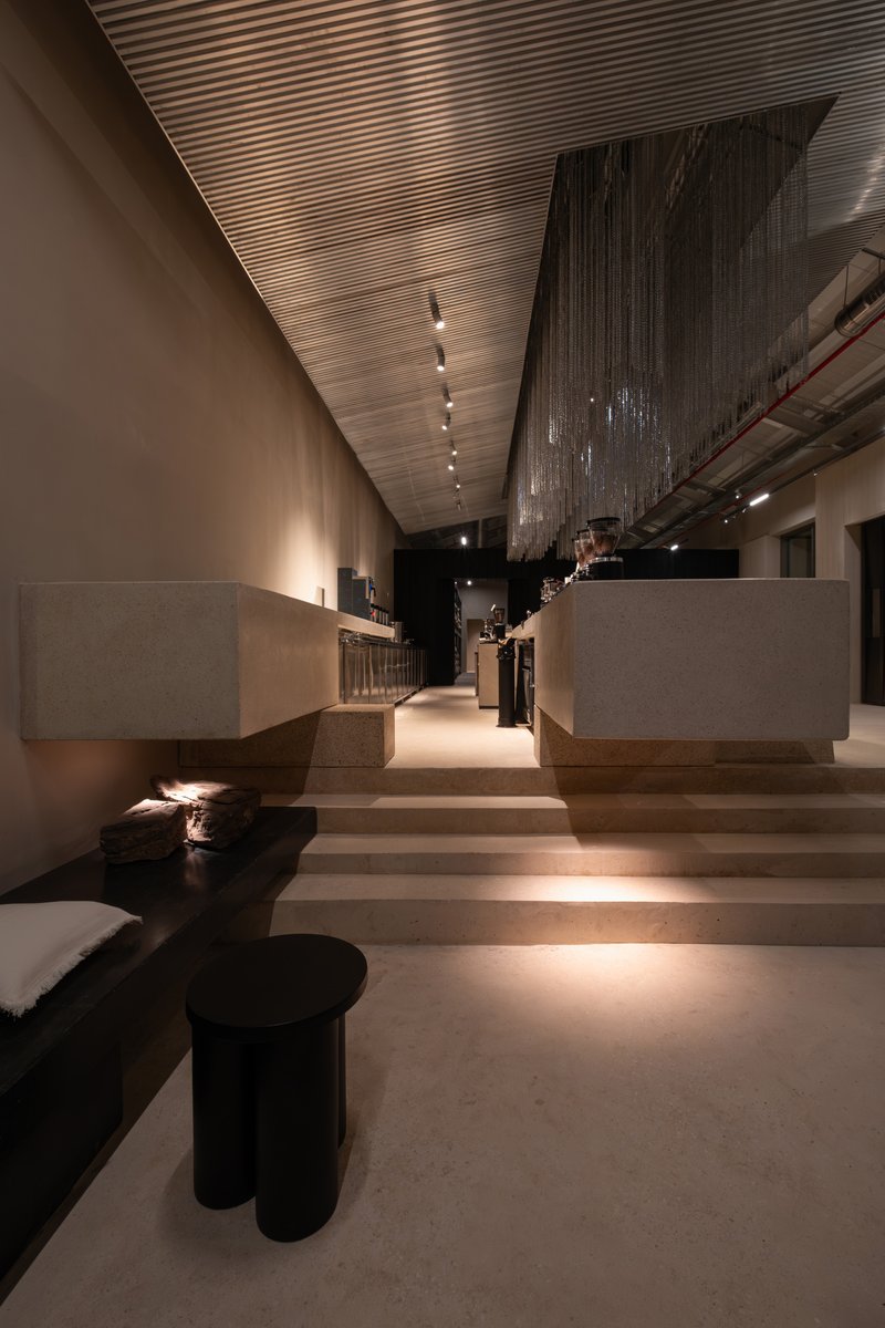 Stepped seating area with terrazzo platforms and slatted ceiling under ambient evening lighting