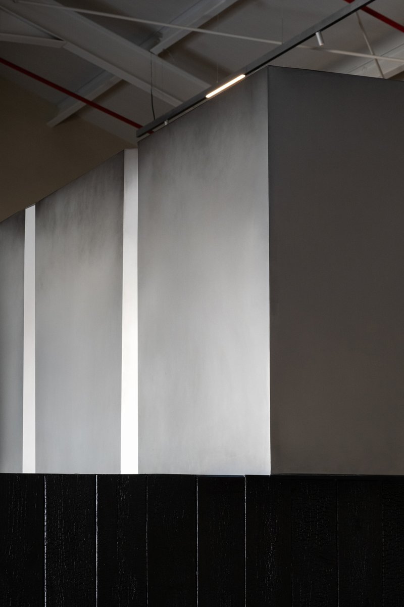 Interior wall detail with vertical grey panels separated by white reveals and exposed ceiling services above