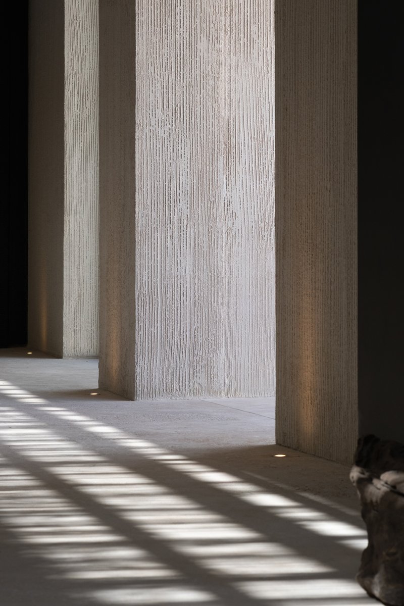 Textured concrete columns with vertical ribbing casting striped shadows across the polished floor in bright sunlight