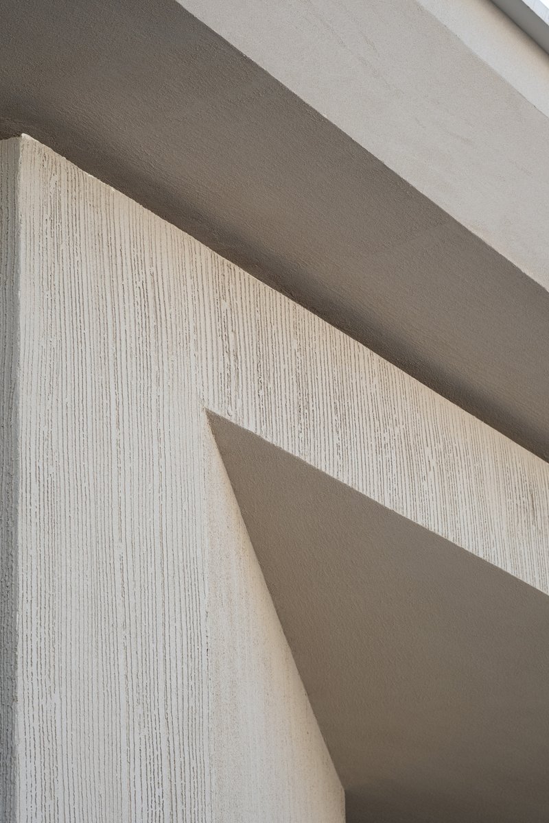 Close-up of vertically striated concrete wall meeting smooth soffit planes under natural daylight