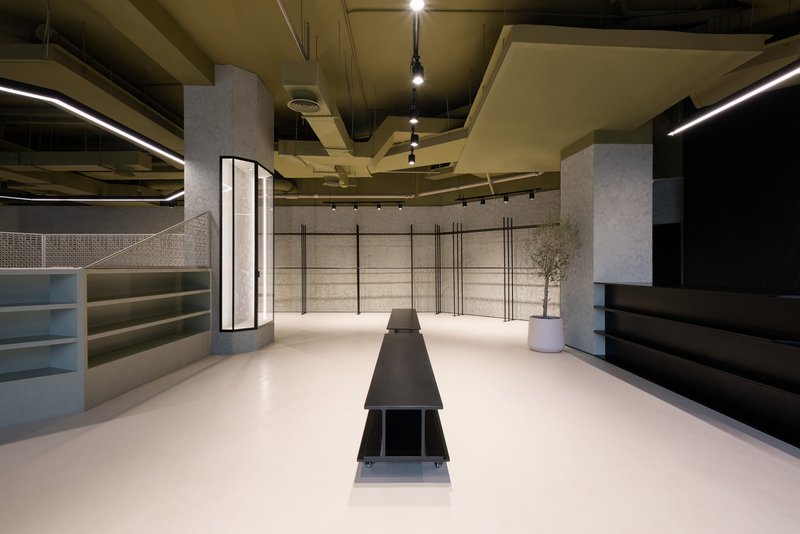 Interior retail space with white resin flooring, glass-framed columns, metal shelving, and a potted olive tree