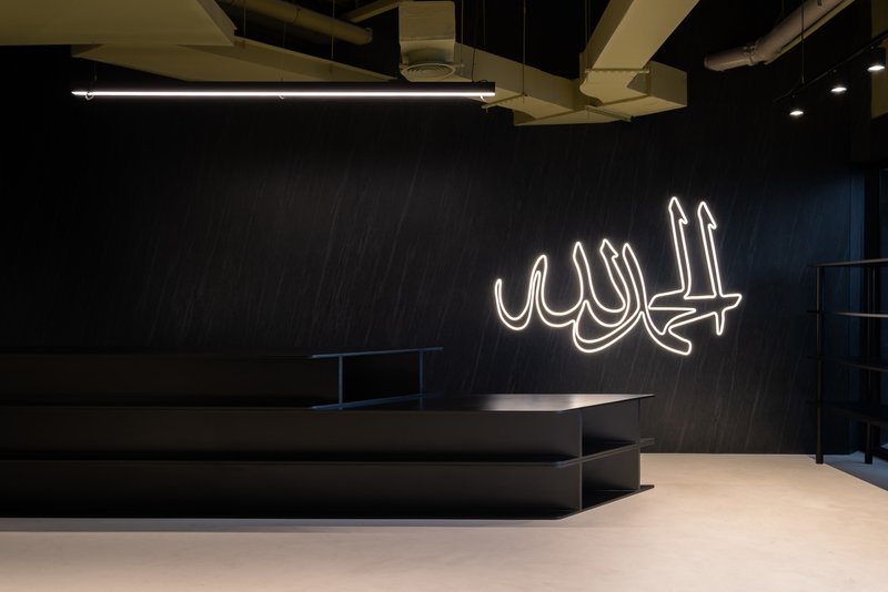 Dark feature wall with white neon Arabic calligraphy above low platform seating and polished concrete floor