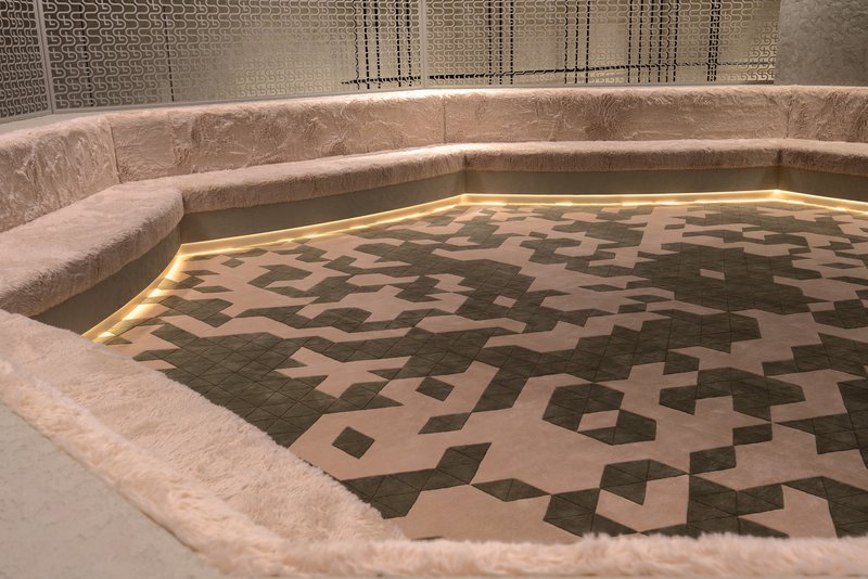 Sunken pool with geometric tiled pattern bordered by plush upholstered seating and perforated metal screens