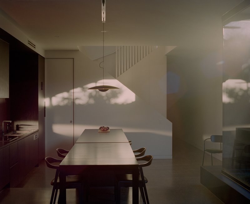 Dining space with suspended pendant lamp casting shadow patterns across white walls in afternoon light