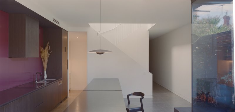Kitchen with dark timber cabinetry and pendant light beside a white partition wall with curved shadow