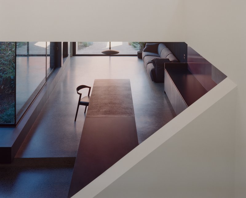 View down through ceiling aperture to lower level living space with polished concrete floor and low couch