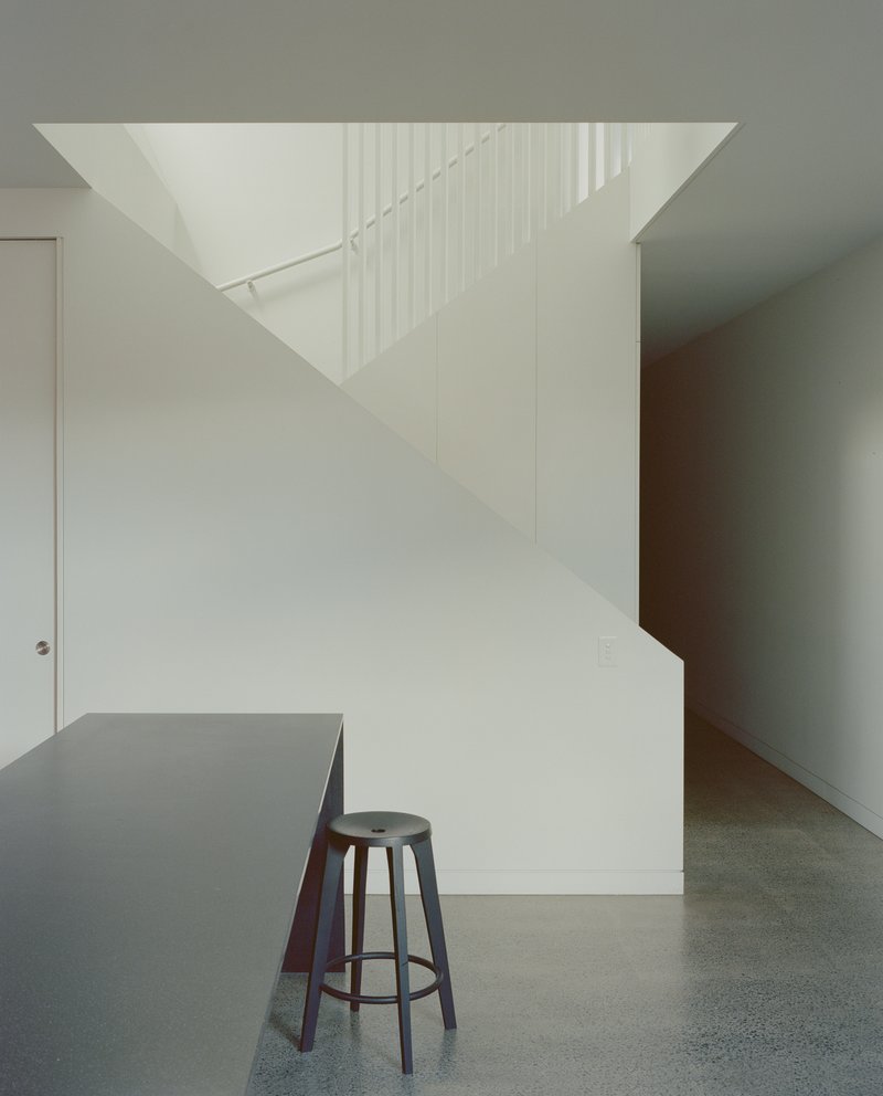 White staircase with vertical metal rods as railing rising beside a grey kitchen island with stool
