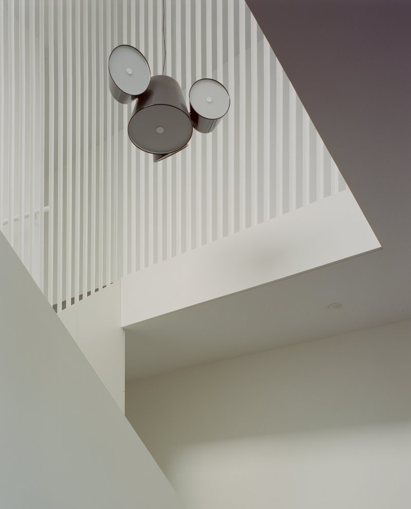 Looking up through stairwell void at cluster of three drum pendant lights against vertical rod railings