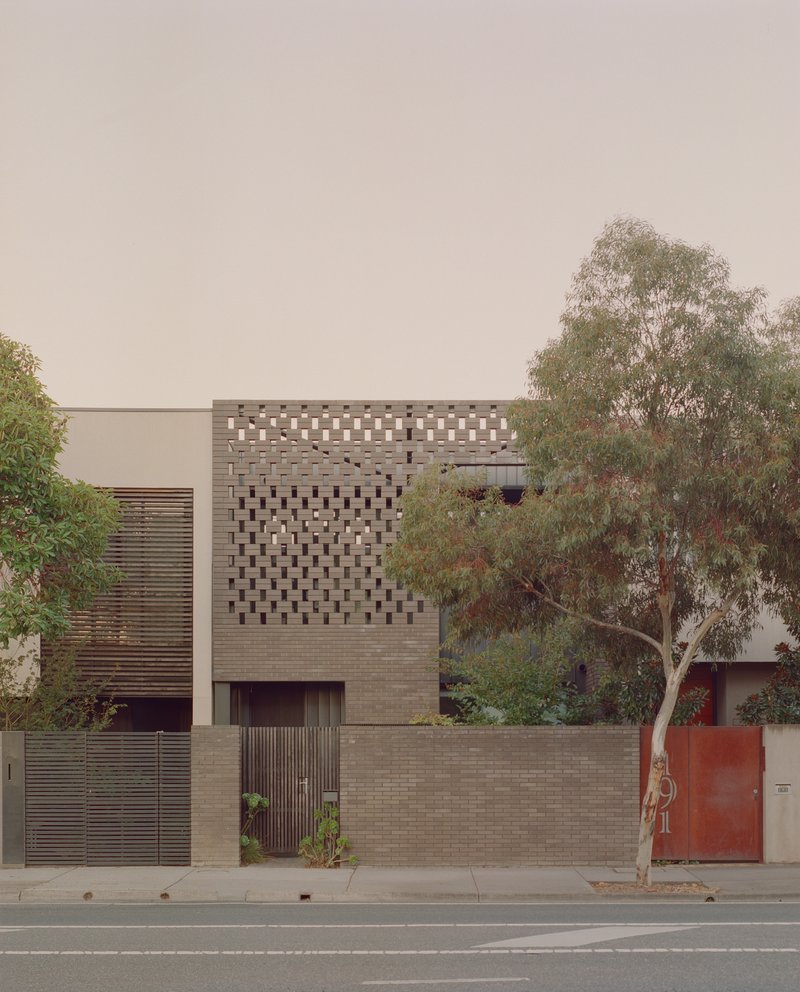 Street facade with perforated brick screen above a timber-slatted gate and planted boundary wall