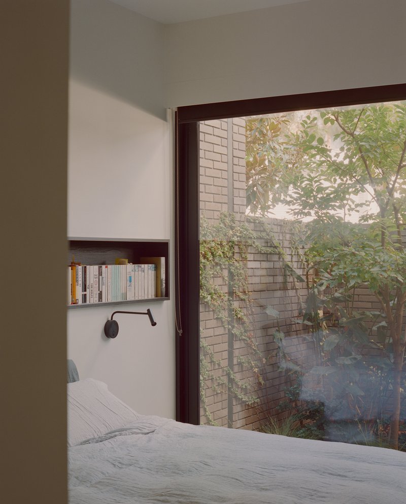 Bedroom corner with recessed shelf and full-height window overlooking a brick courtyard wall with tree