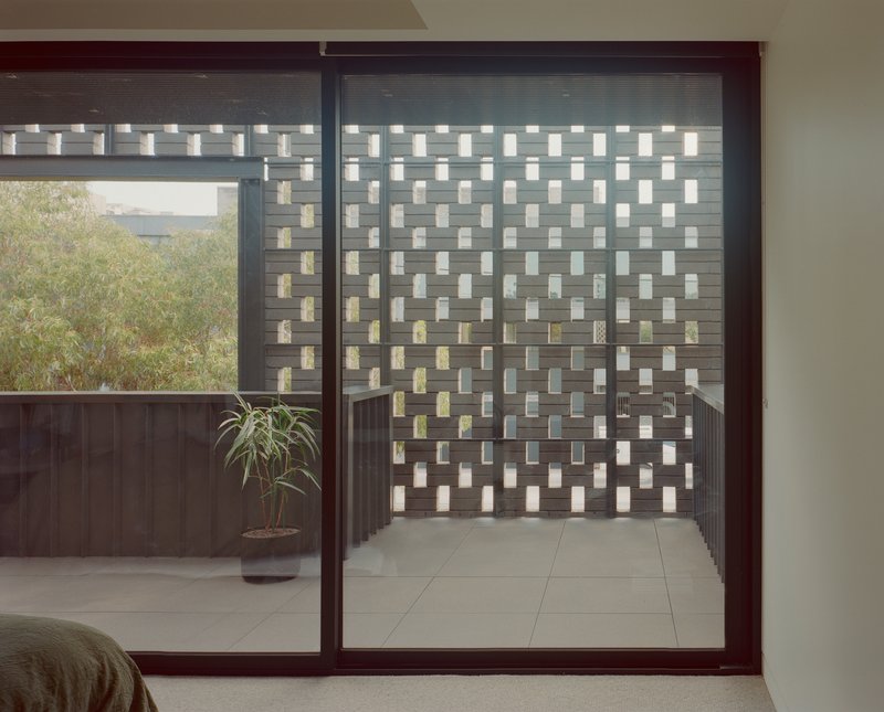 Sliding glass door opening to courtyard with chequered privacy screen and potted plant in diffused daylight