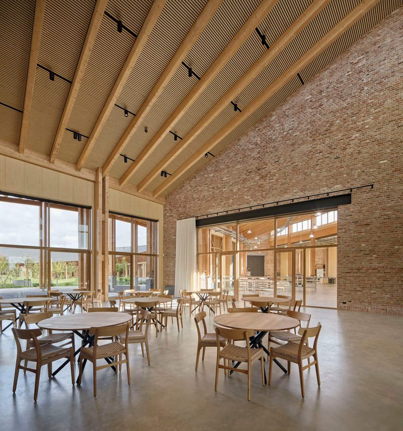 Dining hall interior with curved timber ceiling, brick wall and large windows overlooking the landscape