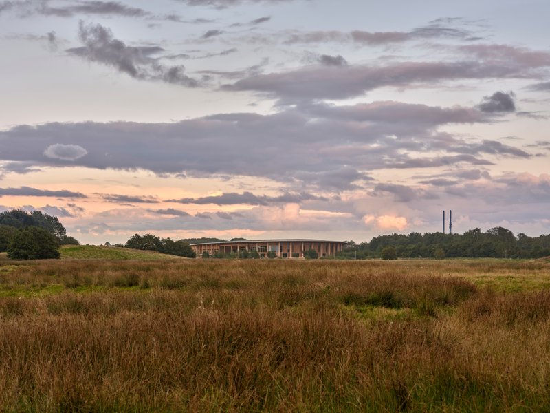 Distant view of the oval building across a wild meadow at dusk