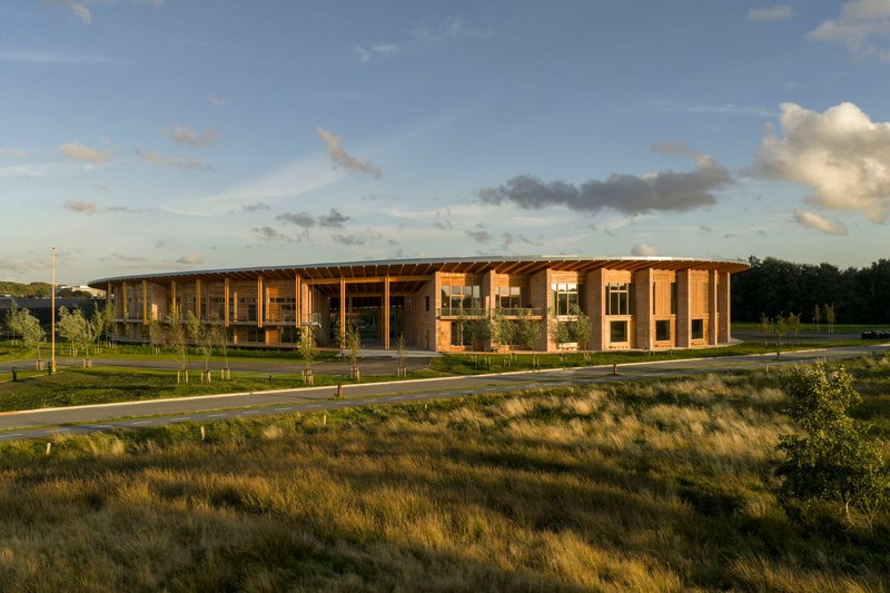 Timber colonnade and glazed facade viewed across native grasses at dusk