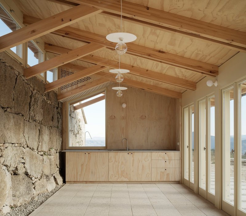 Interior kitchen with plywood cabinetry, exposed timber beams and original granite wall adjacent to glazed doors
